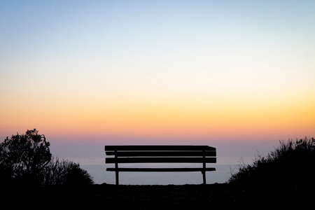 Empty bench overlooking a calm horizon at sunset, with soft light and open space.