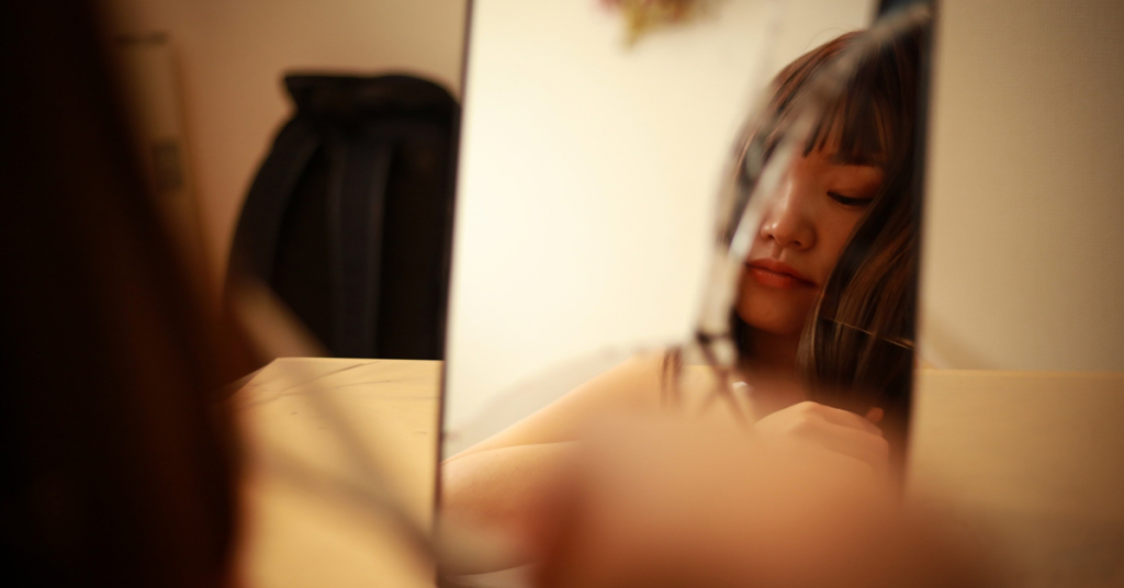 Woman reflected in a cracked mirror, eyes closed, conveying quiet introspection and self-reflection.